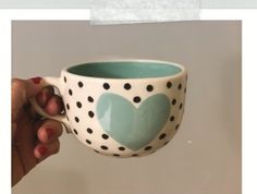 a hand holding a polka dot coffee cup with a heart painted on the outside and inside