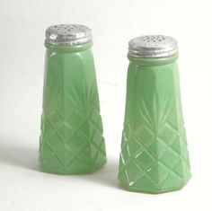 two green glass salt and pepper shakers on a white surface with a silver lid