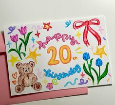 a happy 20th birthday card with a teddy bear and flowers on the front, next to a pink envelope