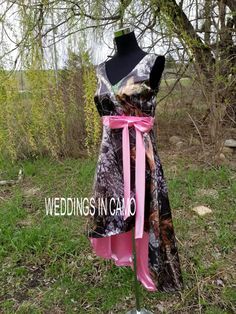 a dress with pink ribbon tied to it sitting on top of a grass covered field