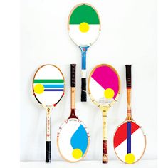 four tennis racquets painted with different colors and shapes on white wall background