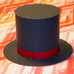 a black top hat with a red ribbon around the brimmed band on an orange and pink background