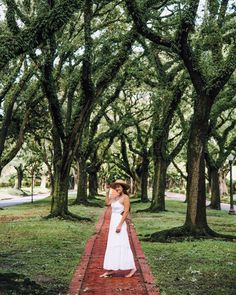 a woman in a white dress standing on a brick path between trees