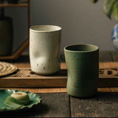 two cups sitting on top of a wooden table next to a green leafy plate