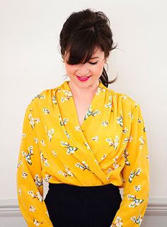 a woman wearing a yellow floral top and black pants with her hands on her hips