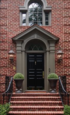 an entrance to a brick building with two planters on the steps and a black door