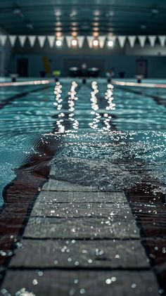 an empty swimming pool with lights reflecting off the water's surface and people in the background