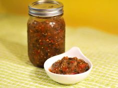 a small white bowl filled with food next to a glass jar full of red stuff