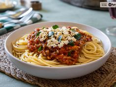 a white bowl filled with pasta and sauce on top of a place mat next to silverware