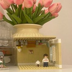 a vase filled with pink tulips sitting on top of a table next to a toy house