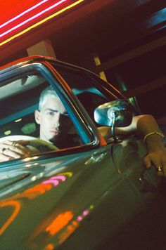 a man sitting in the driver's seat of a car with his hand on the door handle