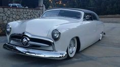 an old white car parked in front of a stone wall