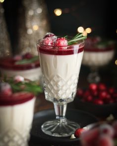 two glasses filled with dessert and garnished with cranberries on a table