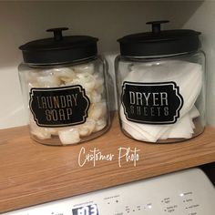 two jars filled with laundry soaps sitting on top of a counter next to a dryer