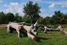 two children playing in an outdoor play area made out of wood logs and plastic barrels