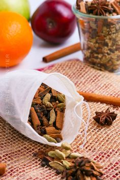 a bag filled with nuts and spices next to an apple, oranges, cinnamon sticks