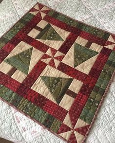 a quilted table topper on a bed with red and green colors in the middle