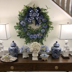 a table topped with blue and white vases next to a wreath on the wall