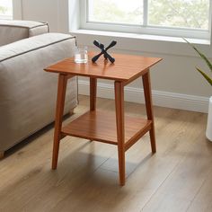 a small wooden table with two glasses on it in front of a couch and window