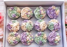 twelve cupcakes in a box decorated with pastel colors and flower decorations on top