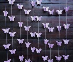 purple paper butterflies hanging from strings on a wooden wall with string attached to the fence