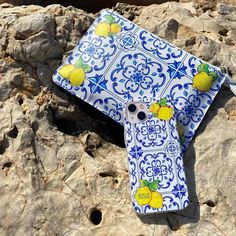 a blue and white ceramic cross with lemons on it sitting on some rocks by the water