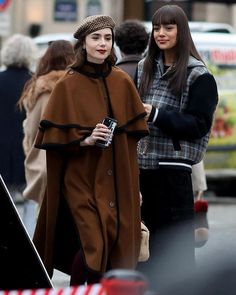 two women are walking down the street in coats and hats, one is holding a camera