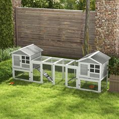 two chicken coops sitting in the grass next to a brick wall and fenced area