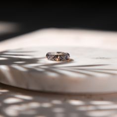 a ring sitting on top of a white plate next to a leafy plant shadow