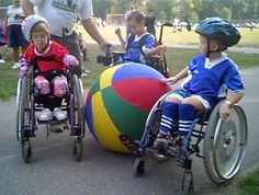 two young boys in wheelchairs are playing with large balls