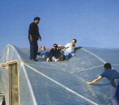 four men are on the roof of a building and one man is falling off his skateboard