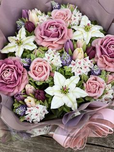 a bouquet of pink roses and white lilies on a wooden table with purple ribbon