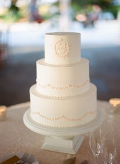 a white wedding cake sitting on top of a table next to wine glasses and silverware