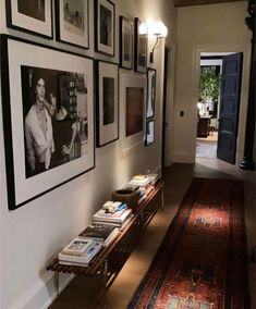 a long hallway with many framed pictures on the wall and an area rug in front of it