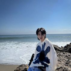 a woman sitting on rocks near the ocean