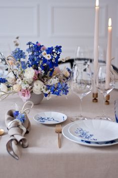 the table is set with blue and white plates, silverware, and flowers in vases