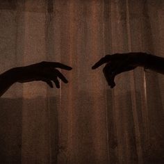 two hands reaching out to each other in front of sheered curtains, with the light shining on them