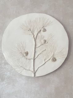 a white ceramic plate with pine cones and needles on the side, sitting on a gray surface