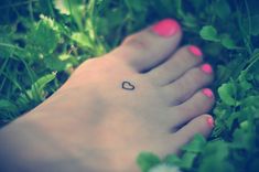 a woman's foot with a small heart tattoo on her left foot and green grass in the background