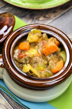 a close up of a bowl of stew on a table with plates and spoons