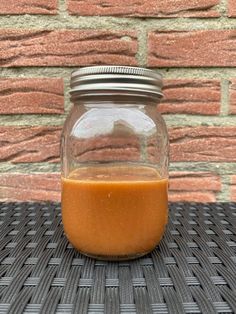 a glass jar filled with orange liquid sitting on top of a wicker table next to a brick wall