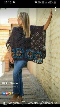 a woman standing next to a wall wearing a crocheted shawl