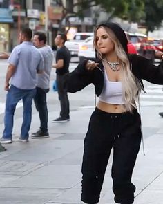 a woman standing on the sidewalk with her arms spread out and wearing black sweatpants