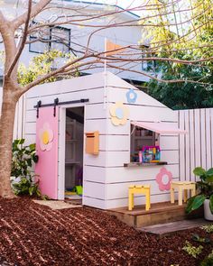 a small pink and yellow play house next to a tree