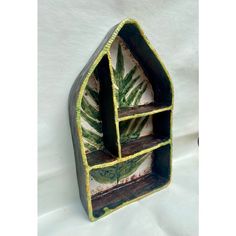 a green and white shelf with two plants on it's sides, sitting against a white background