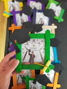 a person holding up a frame made out of construction paper with graduation caps on it