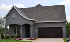 a gray house with two garages and flowers in the front yard