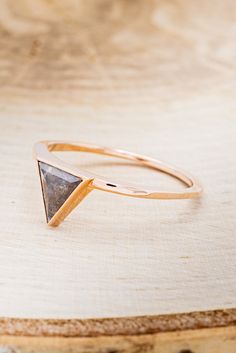 a gold ring with a triangle shaped stone in it on top of a piece of wood