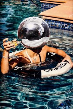 a woman in a pool with a disco ball on her head and a drink in her hand