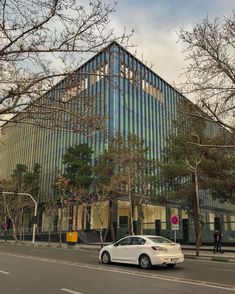 a white car is parked in front of a large glass building with trees on both sides